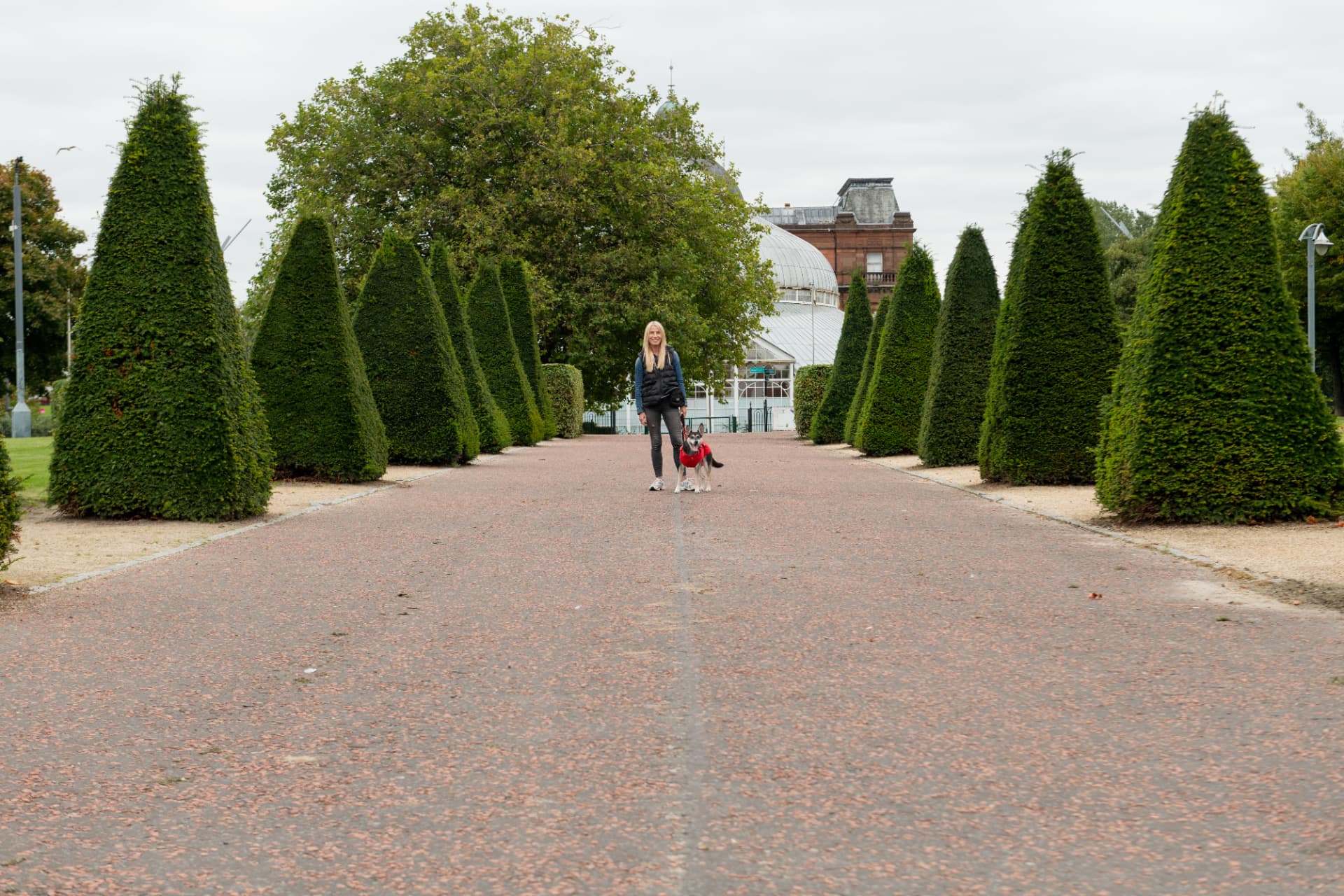 Behaviour consultant Helen Hutcheson walking a dog along a tree-lined Glasgow park path